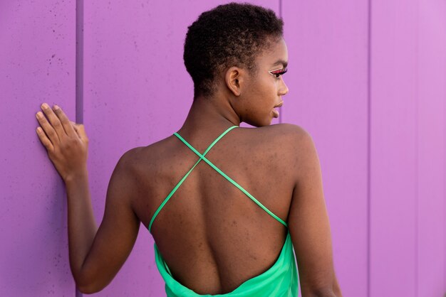 Foto vista traseira de uma mulher negra em um vestido verde elétrico em frente a um fundo lilás