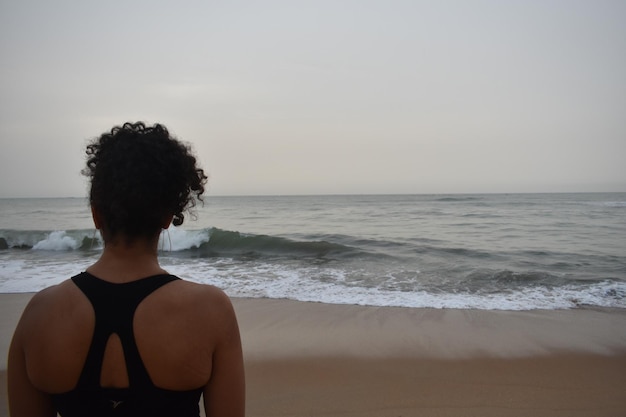 Foto vista traseira de uma mulher olhando para a praia contra o céu durante o pôr-do-sol