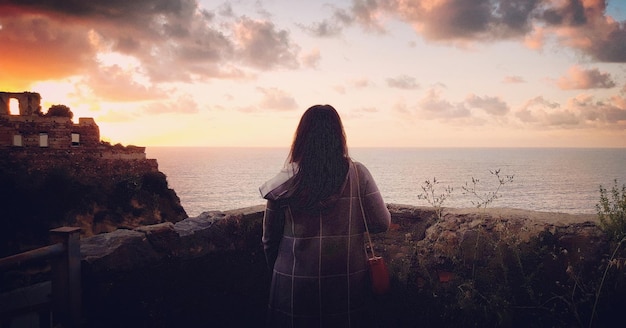Foto vista traseira de uma mulher olhando para a vista do mar durante o pôr-do-sol