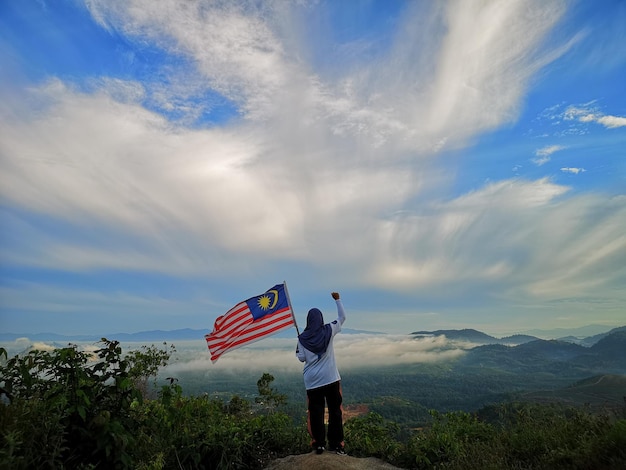 Vista traseira de uma mulher segurando uma bandeira de pé na montanha contra o céu