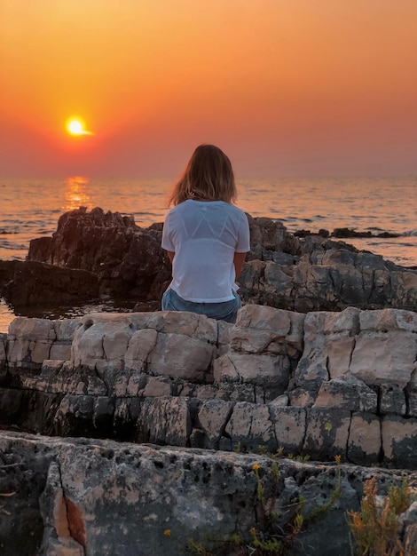 Foto vista traseira de uma mulher sentada em uma formação rochosa contra o céu durante o pôr-do-sol