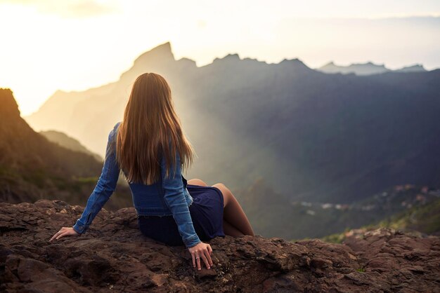 Foto vista traseira de uma mulher sentada em uma rocha contra uma montanha