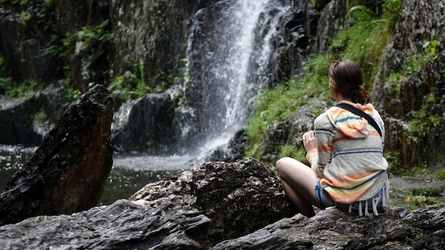 Vista traseira de uma mulher sentada em uma rocha na floresta