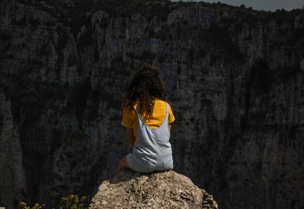 Foto vista traseira de uma mulher sentada em uma rocha