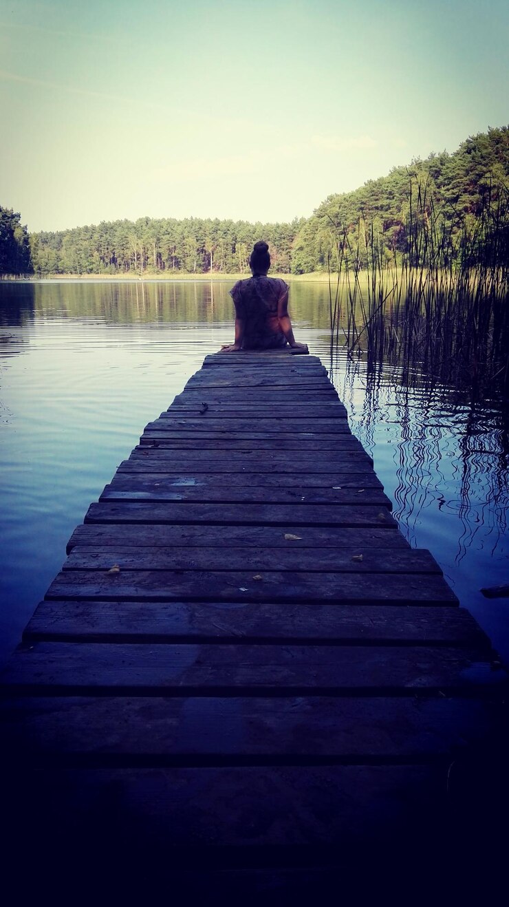Foto vista traseira de uma mulher sentada no cais sobre o lago na floresta