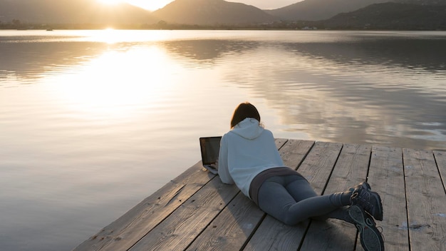 Foto vista traseira de uma mulher sentada no lago contra o céu durante o pôr-do-sol