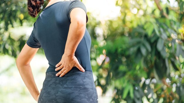 Foto vista traseira de uma mulher sofrendo de dor nas costas enquanto estava de pé no parque
