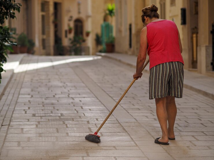 Foto vista traseira de uma mulher varrendo um beco no meio de edifícios na cidade