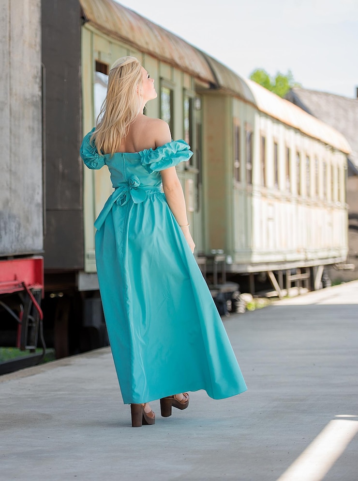 Foto vista traseira de uma mulher vestindo um vestido azul enquanto caminha na plataforma da estação ferroviária