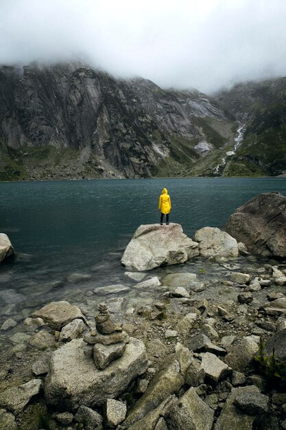 Foto vista traseira de uma pessoa de pé em uma rocha ao lado de um lago contra montanhas