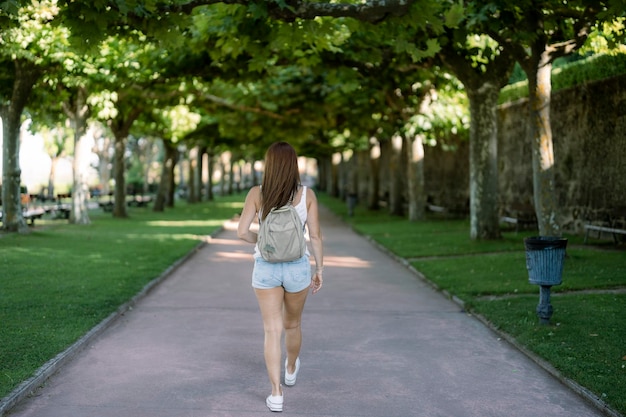 Vista traseira de uma viajante feminina com uma mochila caminhando por uma passarela sombreada