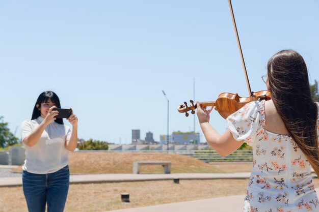 vista traseira de uma violinista feminina criadora de conteúdo tocando violino enquanto era filmada para as mídias sociais