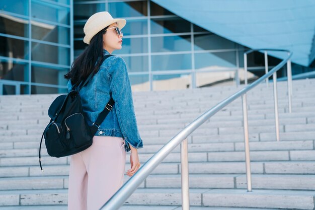 Vista traseira do belo viajante subindo as escadas para entrar no museu em los angeles. estudante universitário asiático indo para o prédio de ensino. jovem no estilo de vida da américa.