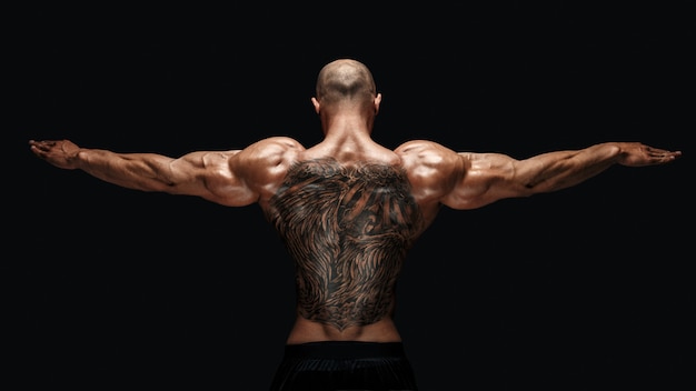 Vista traseira do bodybuilder tattoed com braços estendidos