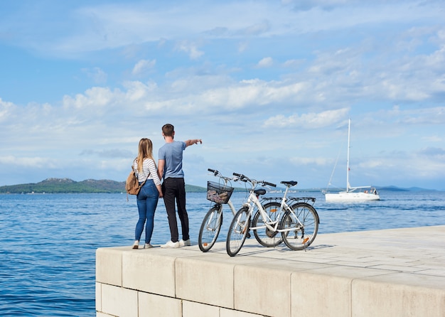 Vista traseira do casal de turistas, homem e mulher em pé em duas bicicletas na calçada de pedra pavimentada alta.