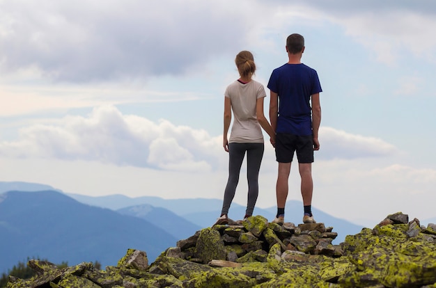 Vista traseira do casal jovem turista de mãos dadas no topo da montanha rochosa