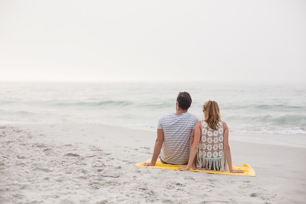 Vista traseira do casal sentado na praia