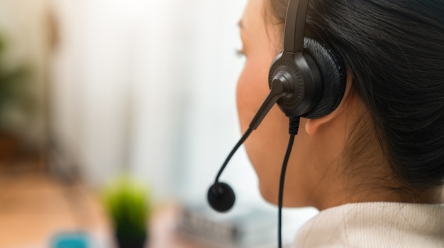 Foto vista traseira do consultor de mulher usando fone de ouvido com microfone da operadora de telefone de suporte ao cliente no local de trabalho. proporção do banner para anúncios.