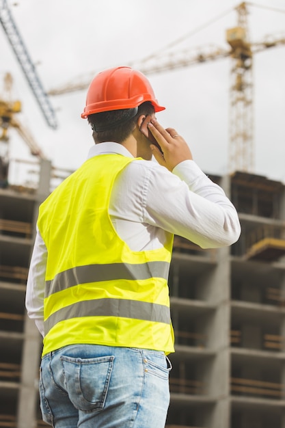 Vista traseira do engenheiro de construção falando ao telefone e olhando para o canteiro de obras