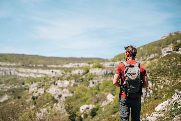 Vista traseira do explorador com mochila admirando o terreno rochoso durante uma caminhada em um dia ensolarado