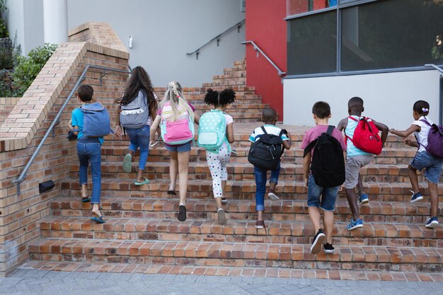 Vista traseira do grupo de diversos alunos com mochilas subindo as escadas juntos na escola