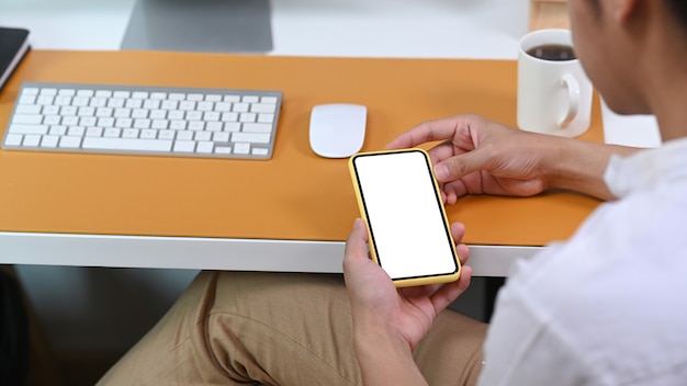 Vista traseira do homem casual sentado na mesa do escritório e usando o telefone inteligente.