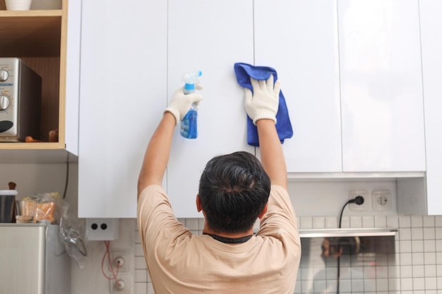 Vista traseira do homem com luvas de proteção limpando armários de cozinha Serviço de limpeza doméstica