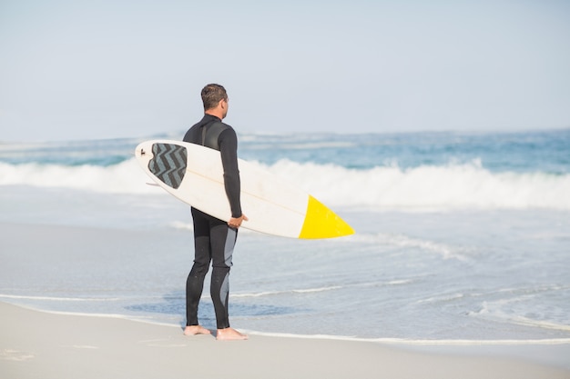 Vista traseira do homem com pé de prancha de surf na praia