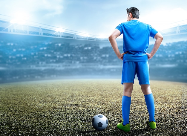 Vista traseira do homem de jogador de futebol asiático em pé com a bola
