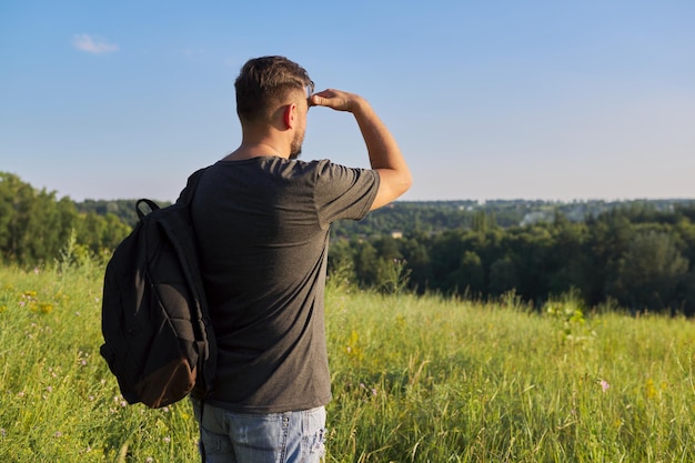 Vista traseira do homem de meia idade com mochila olhando à distância em colinas naturais