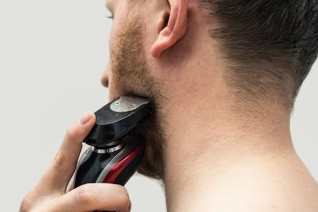 Vista traseira do homem jovem hippie raspando a barba ruiva com um barbeador elétrico. Vista traseira