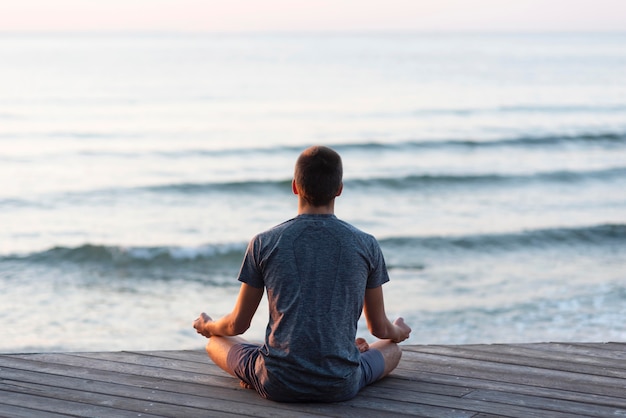 Foto vista traseira do homem meditando na praia