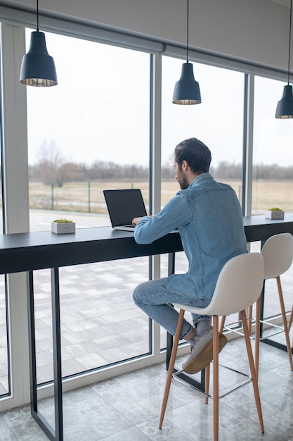 Vista traseira do homem sentado trabalhando no laptop