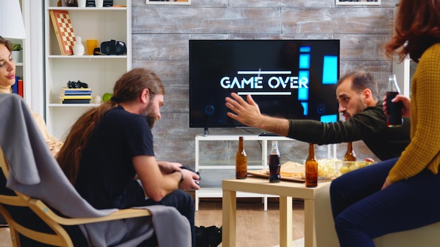 Vista traseira do jogo para mulheres jovens jogando videogame com seus amigos na sala de estar.