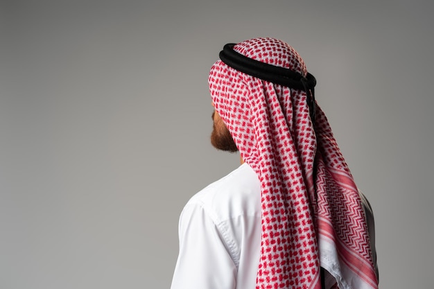 Vista traseira do jovem árabe em pé sobre fundo cinza