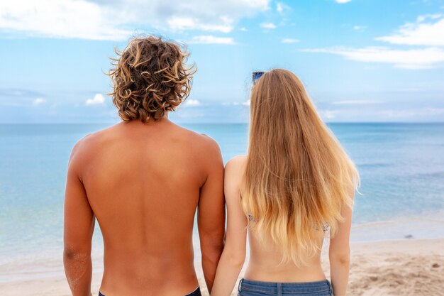 Vista traseira do jovem casal apaixonado na praia e aproveitando o tempo juntos. casal jovem se divertindo em uma costa arenosa.