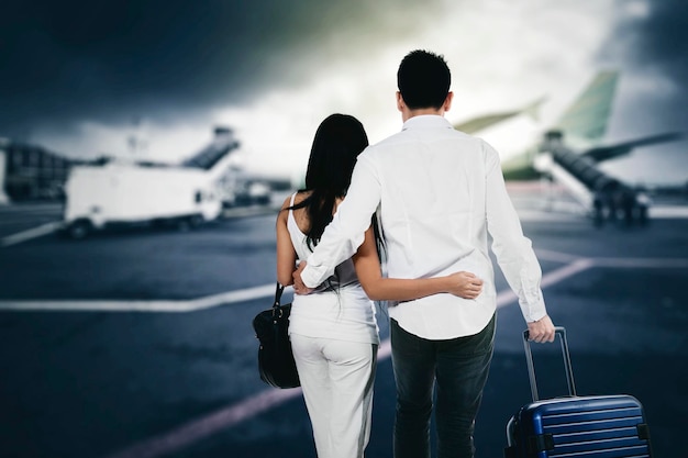 Vista traseira do jovem casal carrega bagagem no aeroporto