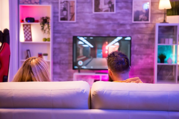 Vista traseira do jovem casal jogando videogame online na televisão. Casal relaxando juntos em casa.