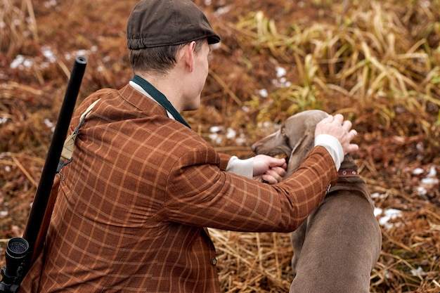 Vista traseira do jovem caucasiano com cachorro cinza sentado no campo esperando o troféu de animal selvagem alvo