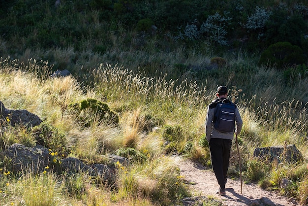 Vista traseira do jovem com mochila e vara caminhando em uma montanha no dia conceito de aventura