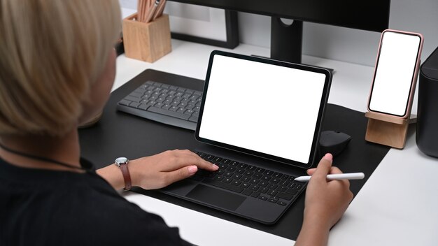 Vista traseira do jovem designer gráfico segurando a caneta stylus e trabalhando na mesa do computador no escritório criativo.