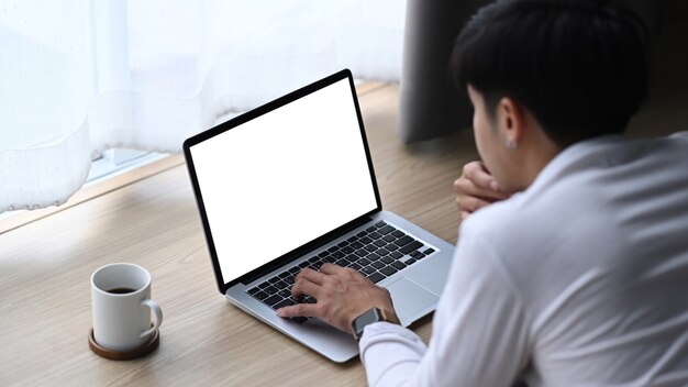 Vista traseira do jovem freelancer deitado no chão de madeira na sala de estar e usando o computador portátil