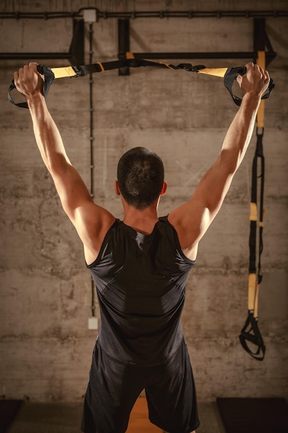 Foto vista traseira do jovem musculoso tendo treino com cintos no ginásio.