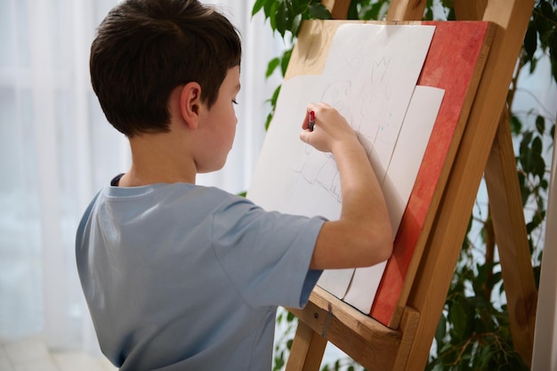 Vista traseira do menino de escola de cabelos escuros caucasiano desenhando em casa, entretenimento de educação infantil, passatempo ou desenho de classe, pintura e conceito de criatividade