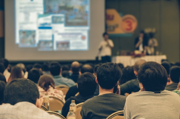 Vista traseira do público ouvindo os palestrantes apresentam o slide no palco da conferência