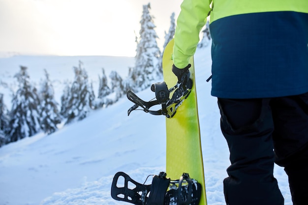 Vista traseira do snowboarder escalando com sua prancha na montagem para sessão de freeride backcountry em