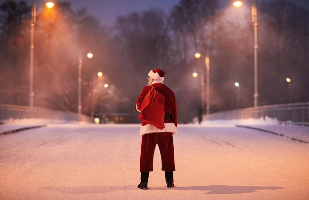 Vista traseira do tradicional papai noel em pé na rua da cidade à noite no espaço de cópia da véspera de natal