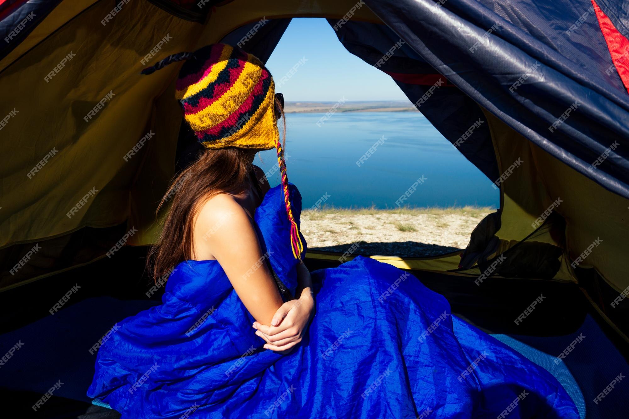 Vista traseira do turista de mulher nua sexy em um chapéu engraçado do  nepal sentado no saco de dormir azul em uma barraca ensolarado bom dia no  lago de montanhas. | Foto