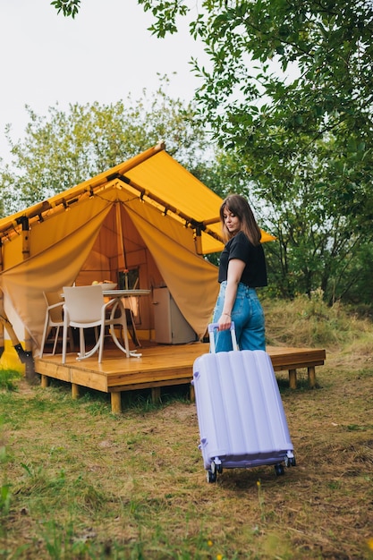 Vista traseira do viajante de mulher com bagagem se movendo para o quarto da aconchegante casa de glamping tenda de acampamento de luxo para férias de verão ao ar livre e férias conceito de estilo de vida