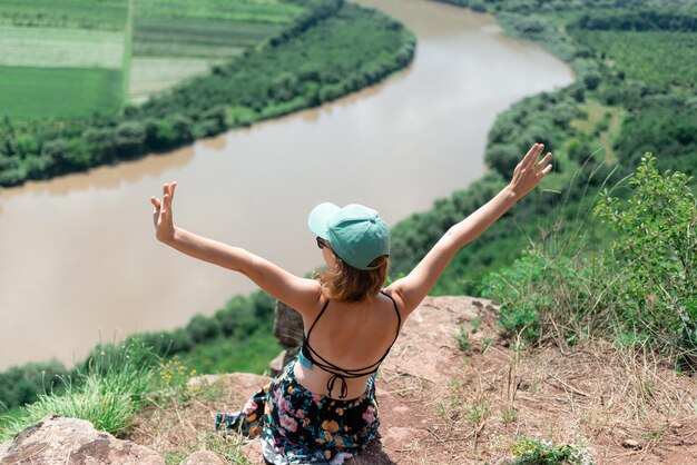 Vista traseira e superior de uma mulher com um chapéu verde sentada com as mãos para cima